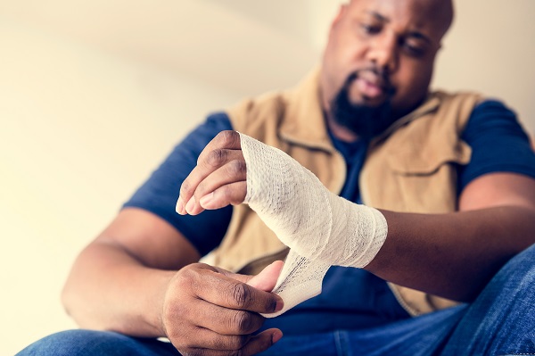 Man in work clothes wraps his injured wrist and hand with a bandage