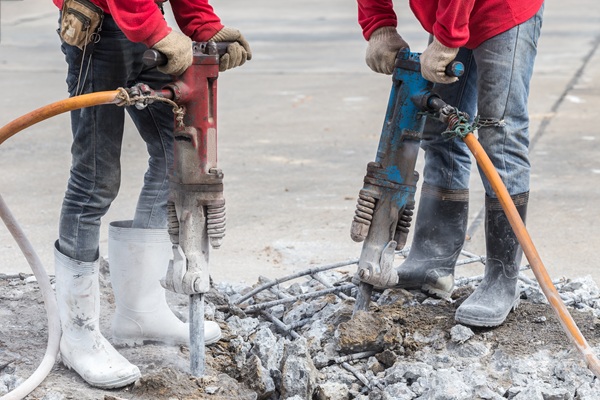 Two construction workers using jackhammers to break concrete at a work site.
